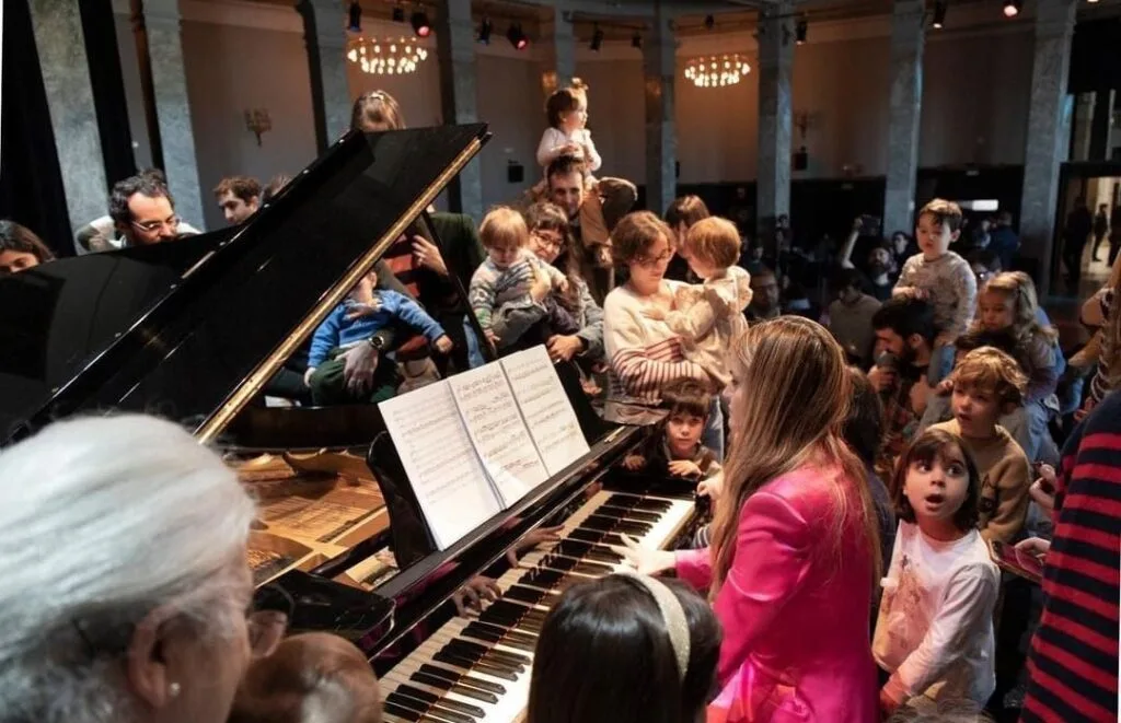 Isabel Dobarro playing the piano surrounded by children at an outreach concert